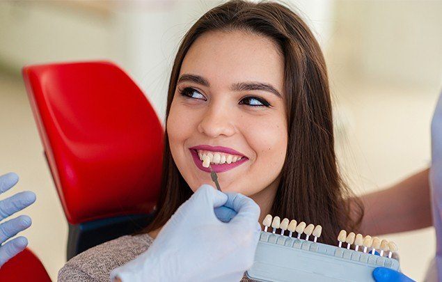 Woman smiling in dental chair next to tooth color chart