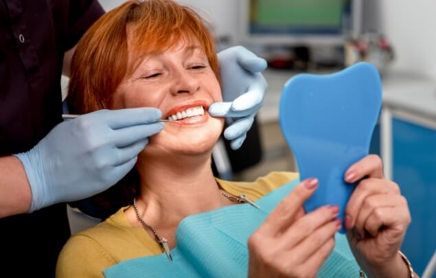 Woman with orange hair in dental chair looking at her smile in mirror