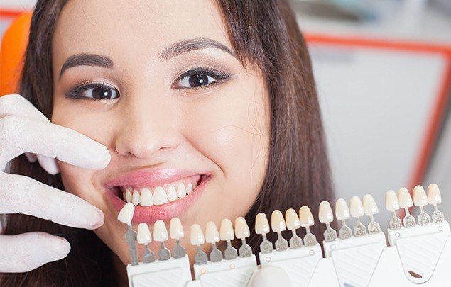 Woman smiling in dental chair next to tooth color chart