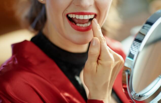 Woman with red lipstick looking at her teeth in mirror