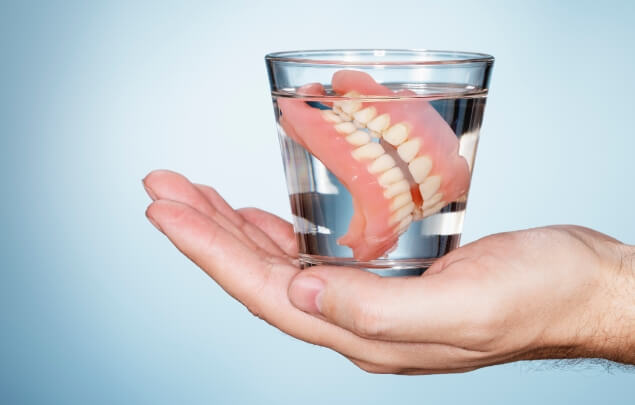 Hand holding a glass of water soaking dentures