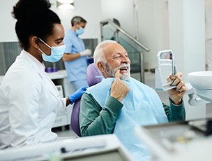 Older man in dental chair pointing to a back tooth next to dentist in white coat