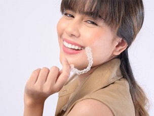 a woman smiling while holding an Invisalign aligner