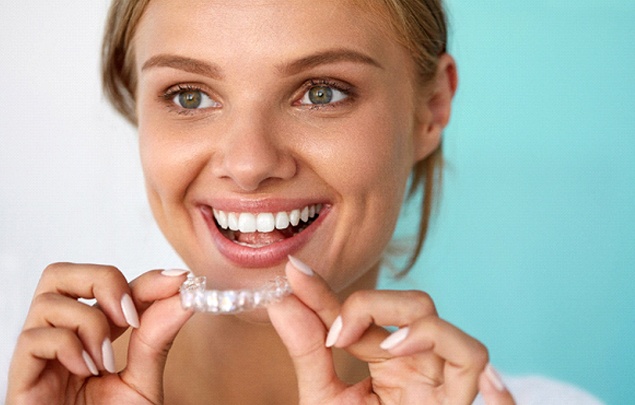 A woman smiling while holding aligner for Invisalign in Selbyville