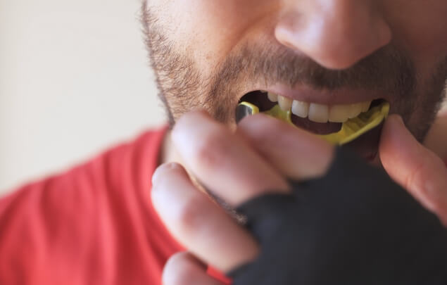 Close up of man placing a yellow mouthguard over his teeth