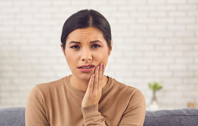 Woman wincing and holding the side of her jaw in pain