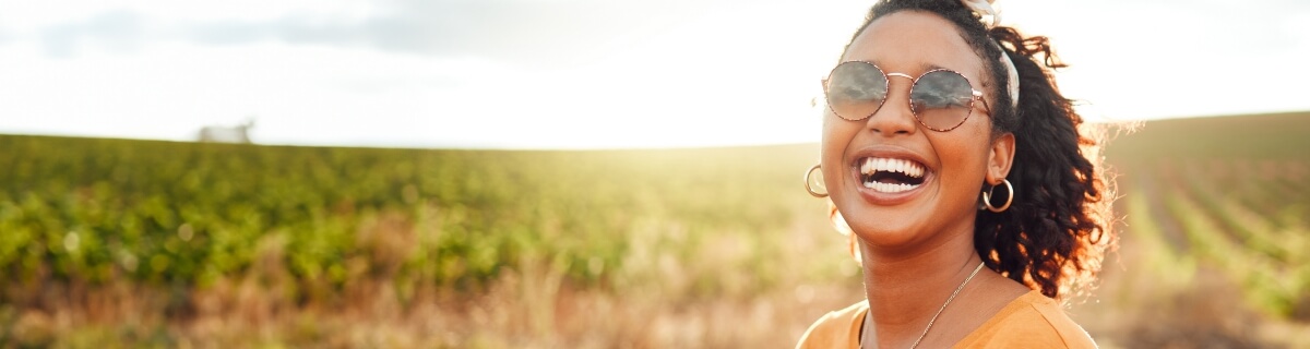 Woman in sunglasses smiling outdoors after root canal treatment in Selbyville