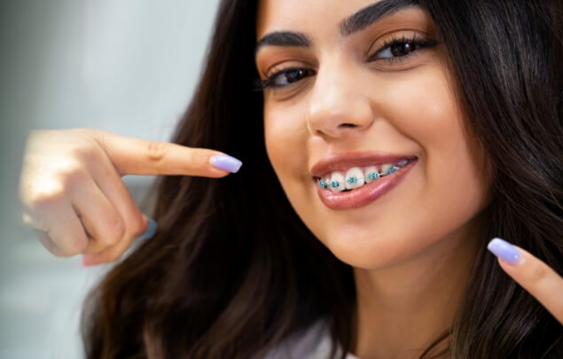 Woman with braces pointing to her smile