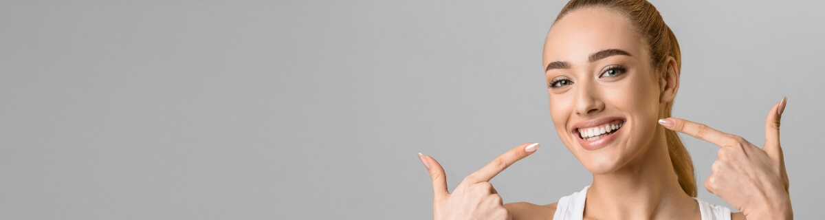 Woman with ponytail pointing to her smile after teeth whitening in Selbyville