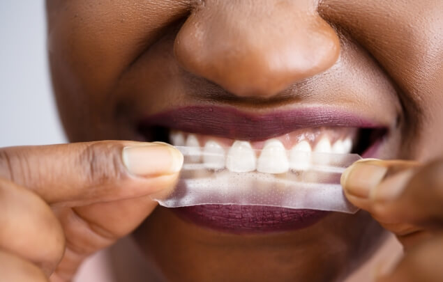 Close up of person placing a whitening strip over their teeth