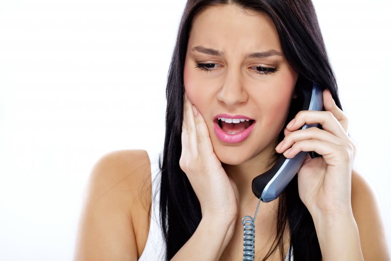 young woman grimacing phoning emergency dentist about toothache