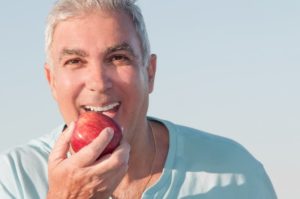 man with implant dentures eating an apple