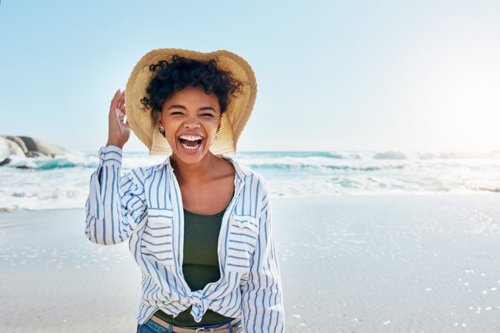 Smiling woman holding onto her hat at the beach