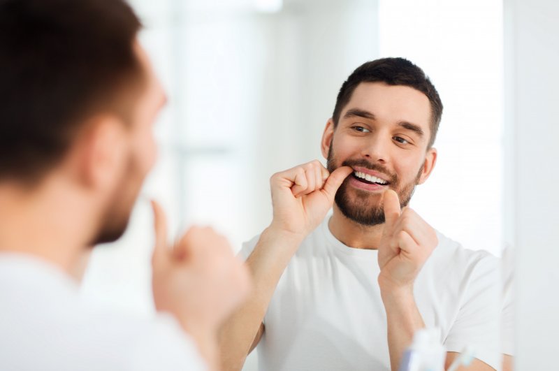 A man flossing his teeth in front of the bathroom mirror