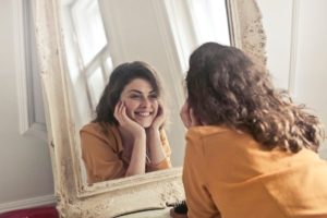 Smiling woman looking at her teeth in mirror