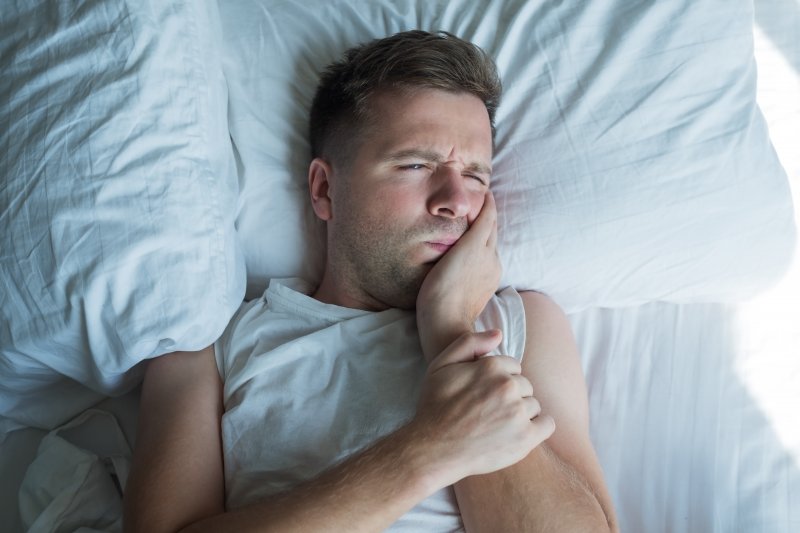 Man lies in bed holding face in pain.