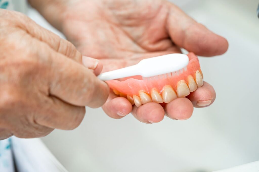 A man cleaning a denture with a toothbrush.